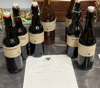 Seven brown bottles of home-brewed beer with brown craft paper labels for the live auction.