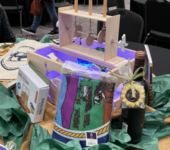 A wooden box features cutouts of Kansas animals and symbols with three wooden bison cutouts on top that rise up and down when spun; a blue light is seen from inside the box, and a birdfeeder, a Kansas flag and a bottle of wine, among other things are included as a table centerpiece.