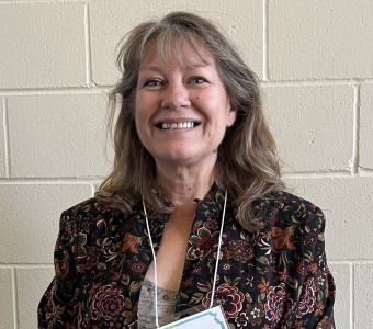 Image of Heather Urich wearing a floral jacket and a nametag on a lanyard.