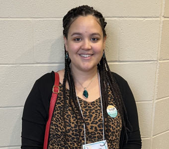 Image of Shai Perry wearing a cheetah print shirt, black cardigan, and nametag on a lanyard.